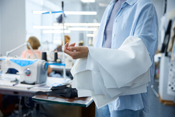 Cobbler carefully reviews cuff pleats near industrial sewing equipment in bright