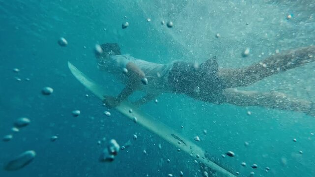 Surfer Performing Duck Dive Underwater Paddling Through Turquoise Water With Surfboard Bubbles And Splash