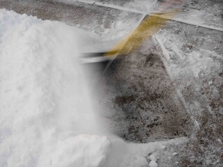 Motion blur of snow shovel pushing through thick white snow on concrete