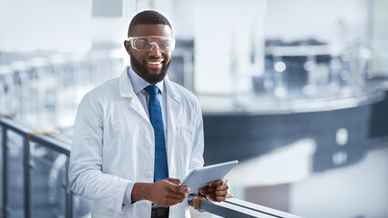A scientist stands in a modern laboratory holding a tablet. They are wearing a white lab coat and safety glasses. The lab is bright and equipped with various scientific instruments.