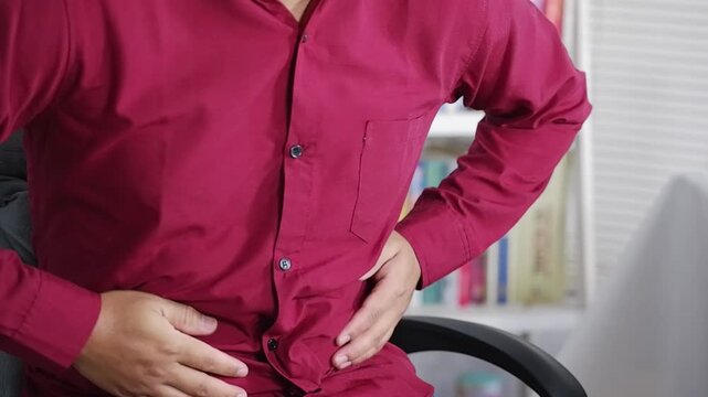 Stomach ache, stomach cramps and a man sitting in a chair at work due to indigestion, diarrhea, or food poisoning. A man has a stomach ache due to constipation, IBS, or abdominal muscle tension at hom