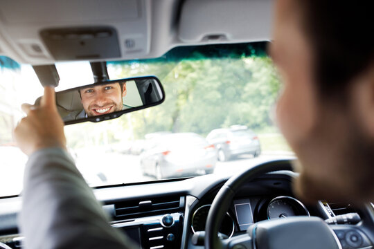 Traveling, way to office, driving car. Millennial caucasian guy in suit with hands on steering wheel, configures mirror, looks in reflection at passenger behind, inside cabin, copy space, cropped