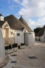 traditional trulli houses with iconic conical stone roofs and whitewashed walls in a narrow paved street of alberobello, puglia, under a blue sky