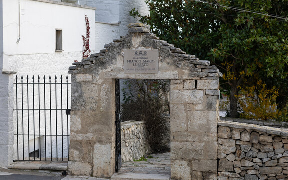 stone entrance to villa comunale franco mario luberto in alberobello, italy, featuring traditional trulli masonry, dry stone walls, and mediterranean greenery
