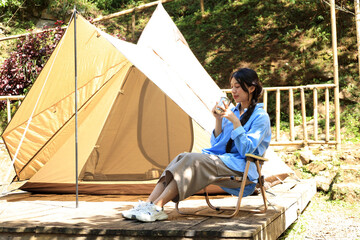 Beautiful Asian Woman Sit on Outdoor Chair In front Of Camping Tent and Drinking a cup of Coffee