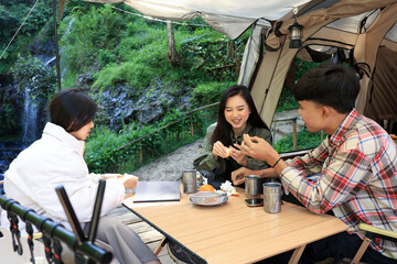 Young Asian Men and Woman Sitting in fron of Camping Tent, Drinking and Eating