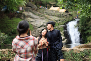 Asian Woman Takes a Photo of Her Friend at a Campsite Next to a River Falls after a Hiking Activity