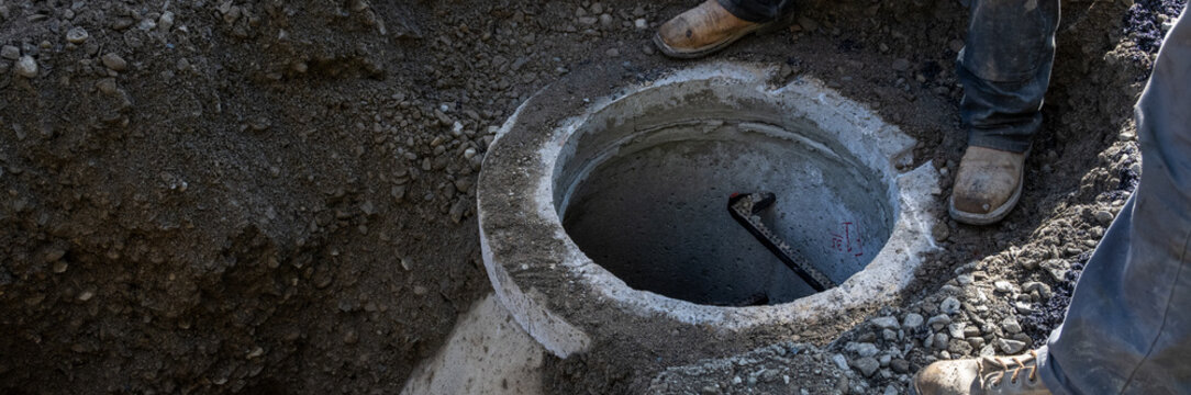 Precast concrete utility hole access point for new public sewer system infrastructure installation project in dug up street, construction workers
