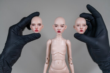 Ball jointed doll body with interchangeable heads held by gloved hands showing detailed customization parts for collectors and hobby artists