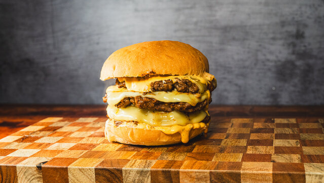 Massive triple deck smash burger with melted cheese dripping down, beautifully presented on a wooden board. Juicy patties, crispy edges, indulgent and perfect for burger lovers.