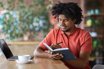 Time Management. Young Black Man Writing In Notepad While Sitting At Table In Cafe, Millennial...