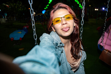 Woman posing on swing sticking tongue out at night © Jordan