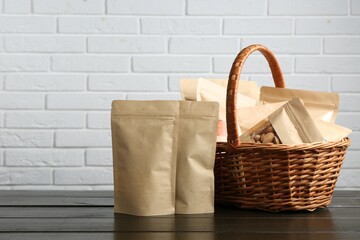 Stand-up pouches with different products in wicker basket on wooden table against white brick...