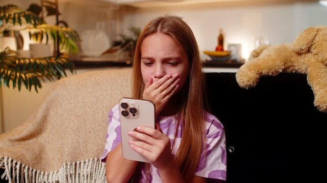 Teenager girl sees defeat alert on smartphone at night home feels disappointed sighs quiet reaction. Caucasian child kid on sofa at evening looks down sad mood types short reply in chat sends emoji