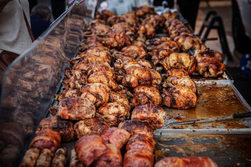 Rotisserie chickens and rolled meats cooking in a display case at a market in france. The golden brown poultry turns on spits in a glass oven at an outdoor stall roasting chickens.