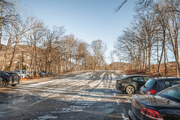 Frozen alpine parking lot with cars, icy asphalt and scattered snow, illustrating dangerous winter driving conditions such as black ice, reduced traction, skidding risk and longer stopping distance.