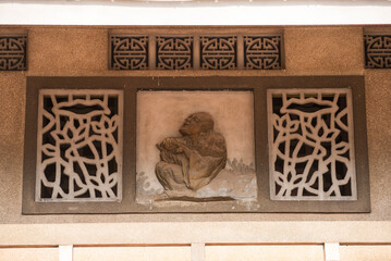 Wall with a statue of a man sitting on a rock. The statue is surrounded by a pattern of leaves