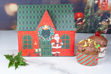 A box shaped like a Christmas house next to small panettone cakes covered in melted chocolate.