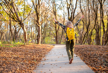 Blonde woman walking in autumn forest on narrow trail with yellow backpack and plaid shirt. Calm outdoor lifestyle supporting mental health