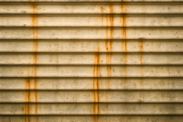 A weathered metal wall with horizontal ridges shows streaks of orange rust and dark stains adding texture and character to the aged industrial surface in soft light