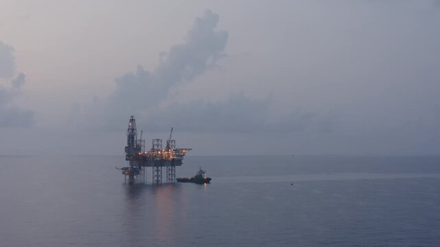 Aerial view from a drone of big jack up offshore drilling oil rig, production platform and supply vessel In the ocean during sunset - Oil and Gas Industry

