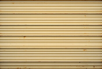 Beige metal wall with horizontal ridges and signs of rust and weathering the surface is textured with parallel lines and appears industrial and aged