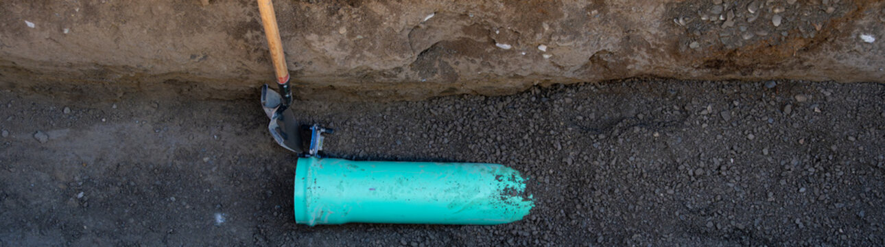 New 8 inch sewer line pipe being installed in trench under the road to build out infrastructure for new housing development construction project
