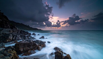 A serene seascape captures a dramatic sunset, with waves crashing against rugged, rocky terrain under moody clouds