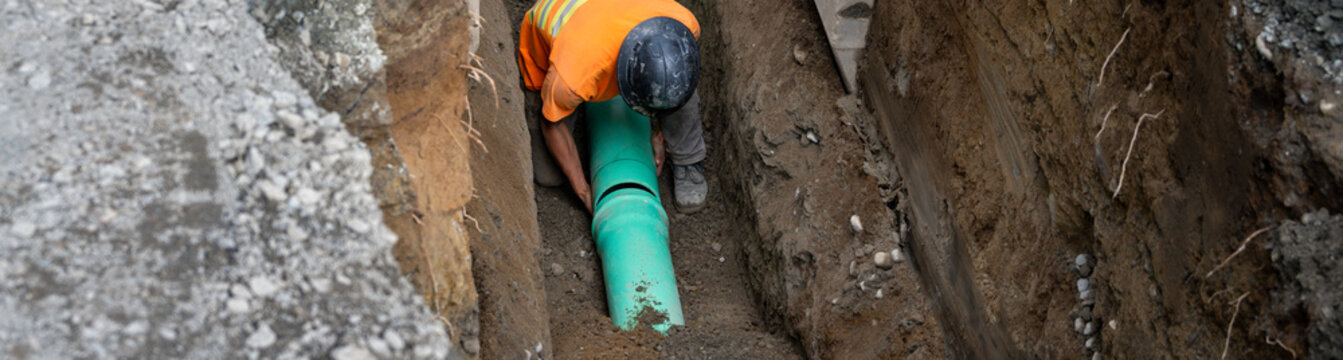 Construction worker in deep trench protected by Trench Box, coffin, while installing new 8 inch sewer line pipe under the road, building out infrastructure for new housing development
