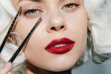 Glamorous beauty portrait of a model with vintage curls, bold red lips, perfect skin, showcasing makeup techniques with brushes.