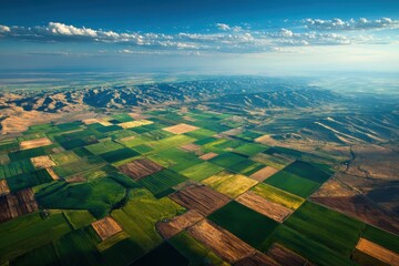 Aerial view shows patchwork of fields, rolling hills, and sky. Use to illustrate agriculture, landscape, or environmental topics.