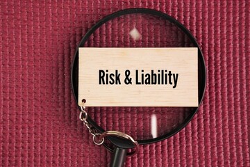 A magnifying glass and a wooden tag with the words Risk and Liability. Liability risk is the...
