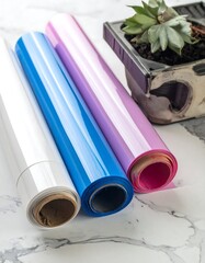 Fototapeta premium Close-up of glossy, colorful film rolls resting on a marble surface next to a succulent plant in a small container