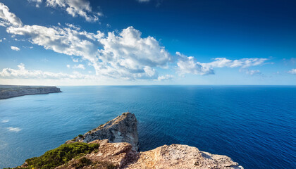 Serene Cliff Overlooking Tranquil Ocean Under Bright Blue Sky With White Clouds