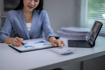 Businesswoman analyzing financial charts and using calculator in office