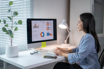 Asian businesswoman analyzing financial charts on computer in modern office