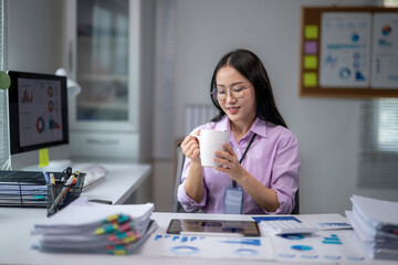 Asian businesswoman drinking coffee and working with financial documents at office desk