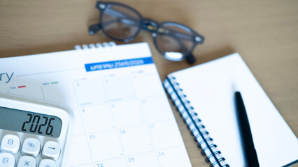 Office desk with calendar, calculator, notebook, and glasses symbolizing business planning, financial organization, and productivity goals for 2026.