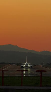 Vertical rear view of a commercial airplane taking off into a golden sunset sky