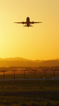 Vertical silhouette of a commercial airplane taking off into a golden sunset sky