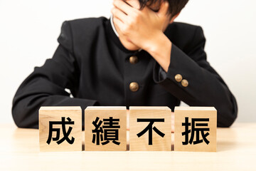 「成績不振」と書かれたブロックと悩む男子学生