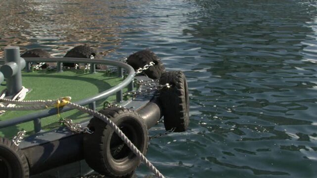 Bow tires on tugboat moored at waterfront pier, bobbing on waves