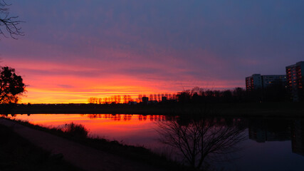 Dramatic urban sunset over a lake with vibrant sky colors and building silhouettes reflecting in the water subtle gradient in Poland