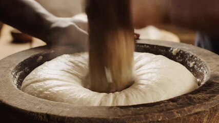 Closeup view of hands rhythmically pounding a traditional staple food likely fufu or similar dough in a large rustic wooden mortar with a pestle showcasing ancient culinary techniques and cultural he.
