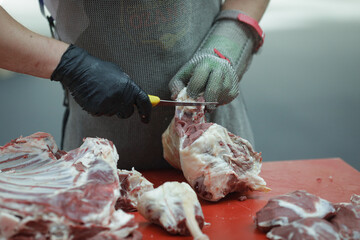 Details with the hands of a butcher, a knife in one and a metal glove in the other, cutting a pork carcass