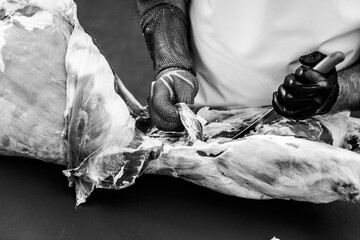 Details with the hands of a butcher, a knife in one and a metal glove in the other, cutting a pork carcass