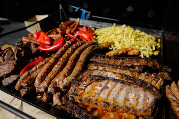 Meat products (mici, pork ribs, sausages, french fries) on an outside charcoal metal grill