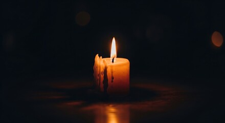 A lit candle glows in the dark, wax melting down the side, warm light against deep black