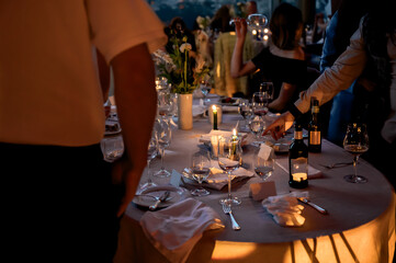Elegant candlelit dinner table at a luxury evening event with wine glasses, floral centerpiece, and guests mingling, capturing a warm, intimate, and sophisticated celebration atmosphere.
