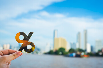 Interest rate and financial percentage concept with hand holding percent symbol over city background. Symbol of finance, investment, banking, loan rates, inflation, economic growth.